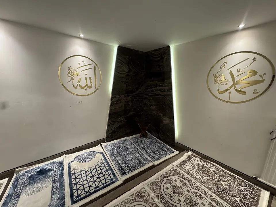 Separater Gebetsraum für Herren (Mescit) im Café Peri Berlin mit Gebetsteppichen und goldener Kalligrafie an der Wand.